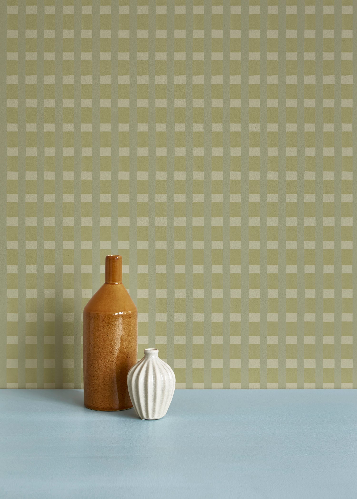 Two ceramic vases against a wallpaper in a gridded check pattern in soft shades of green.