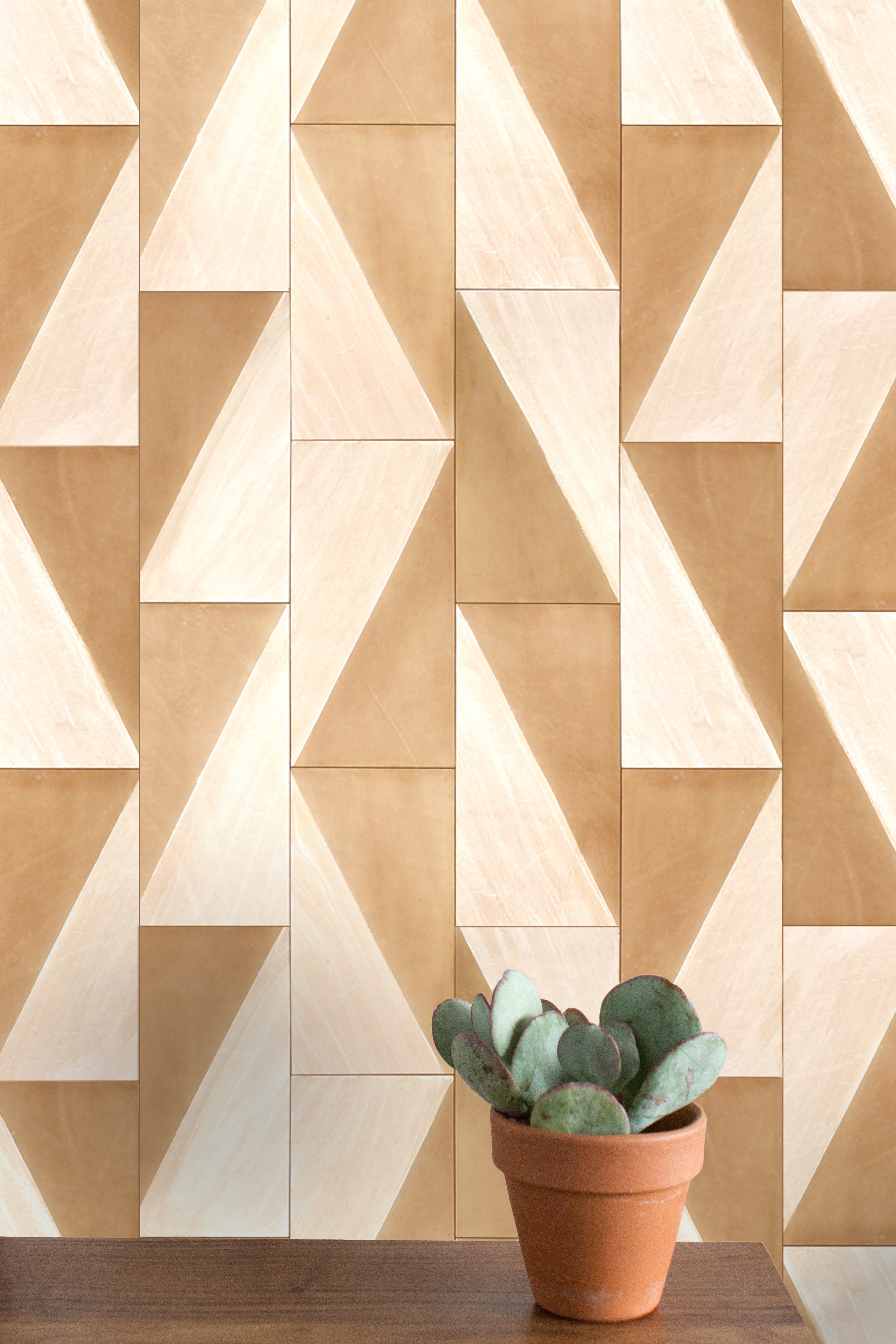 A potted cactus stands in front of a wall papered in leather wall tiles in a repeating geometric print.