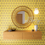 A floating shelf and statement mirror hang on a wall papered in an intricate circular print in yellow, purple and gray.