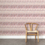 A wooden chair stands in front of a wall papered in a painterly ikat print in shades of purple and pink on a white field.