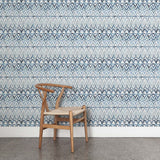 A wooden chair stands in front of a wall papered in a painterly ikat print in shades of blue and navy on a white field.