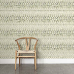 A wooden chair stands in front of a wall papered in a painterly ikat print in shades of green on a white field.