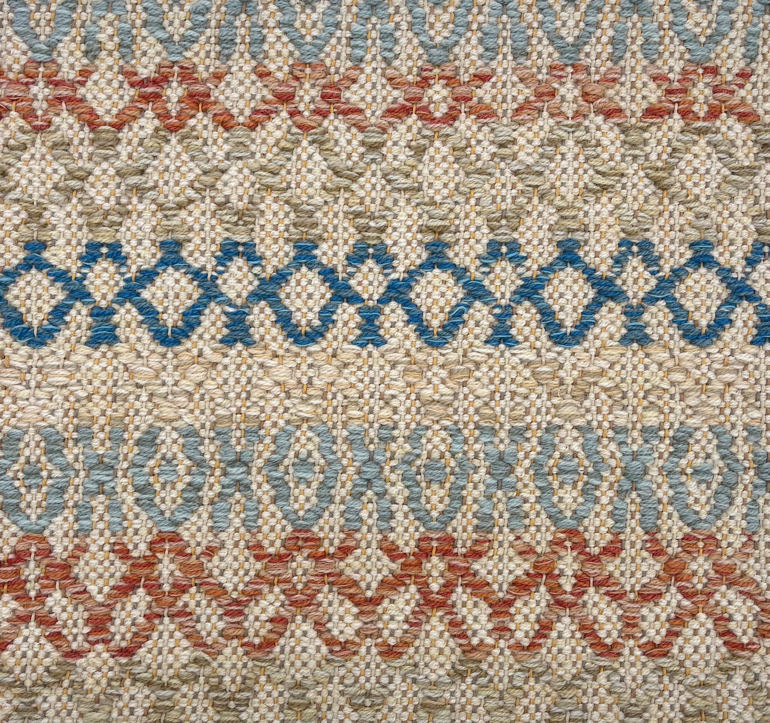 Handwoven rug detail in a lattice stripe design in blue, rust red, sage green and tan. 