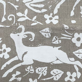 Close-up of fabric in a deer, leaf and flower print in white on a light brown field.