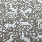 Detail of fabric in a deer, leaf and flower print in white on a light brown field.