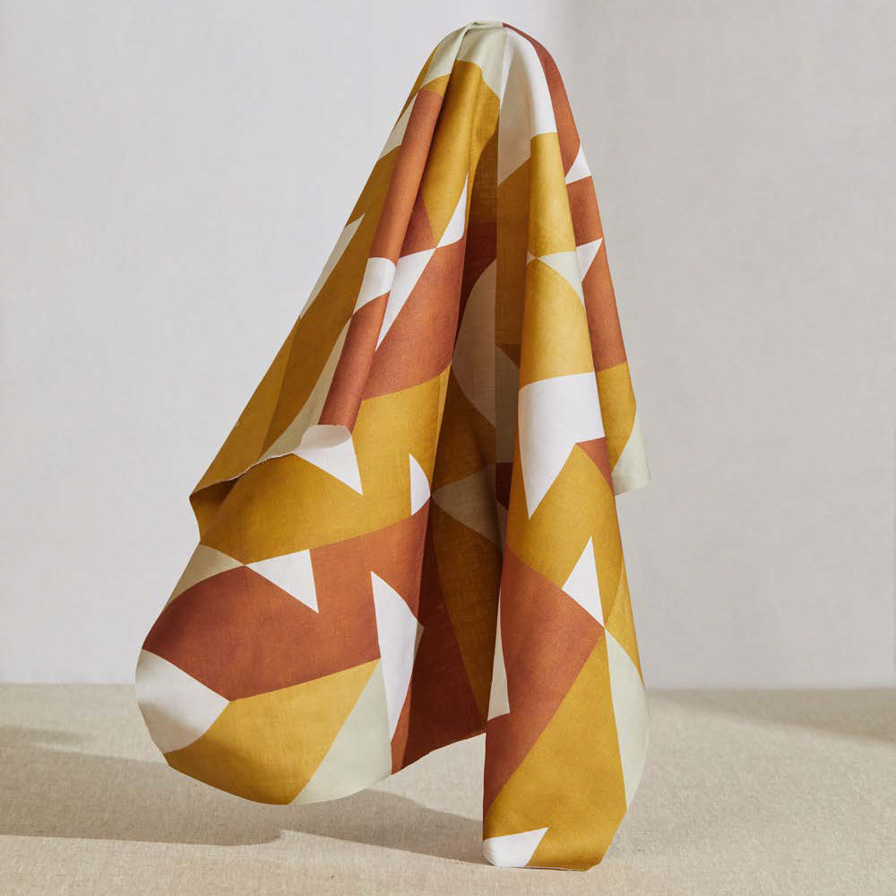 A large piece of draped fabric in a large-scale geometric print in orange and rust on a white field.