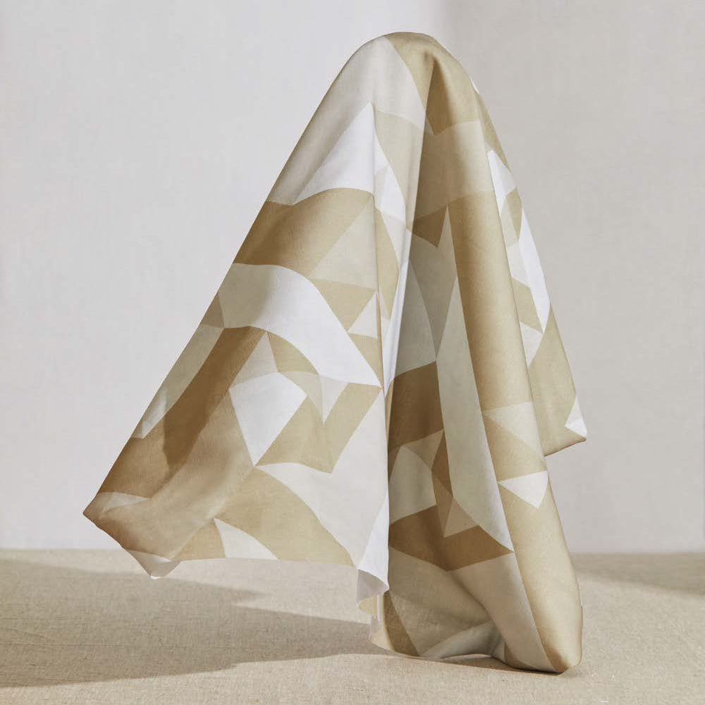 A large piece of draped fabric in a large-scale geometric print in cream and tan on a white field.