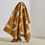 A large piece of draped fabric in a large-scale curvilinear geometric print in sienna on a tan field.