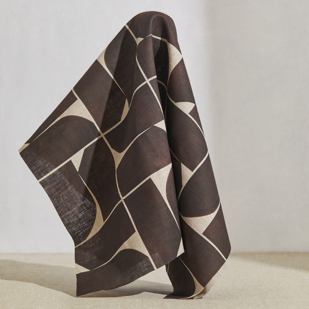 A large piece of draped fabric in a large-scale curvilinear geometric print in brown on a cream field.