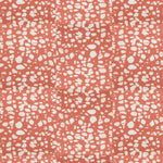 Detail of fabric in a batik splatter print in cream on a coral field.