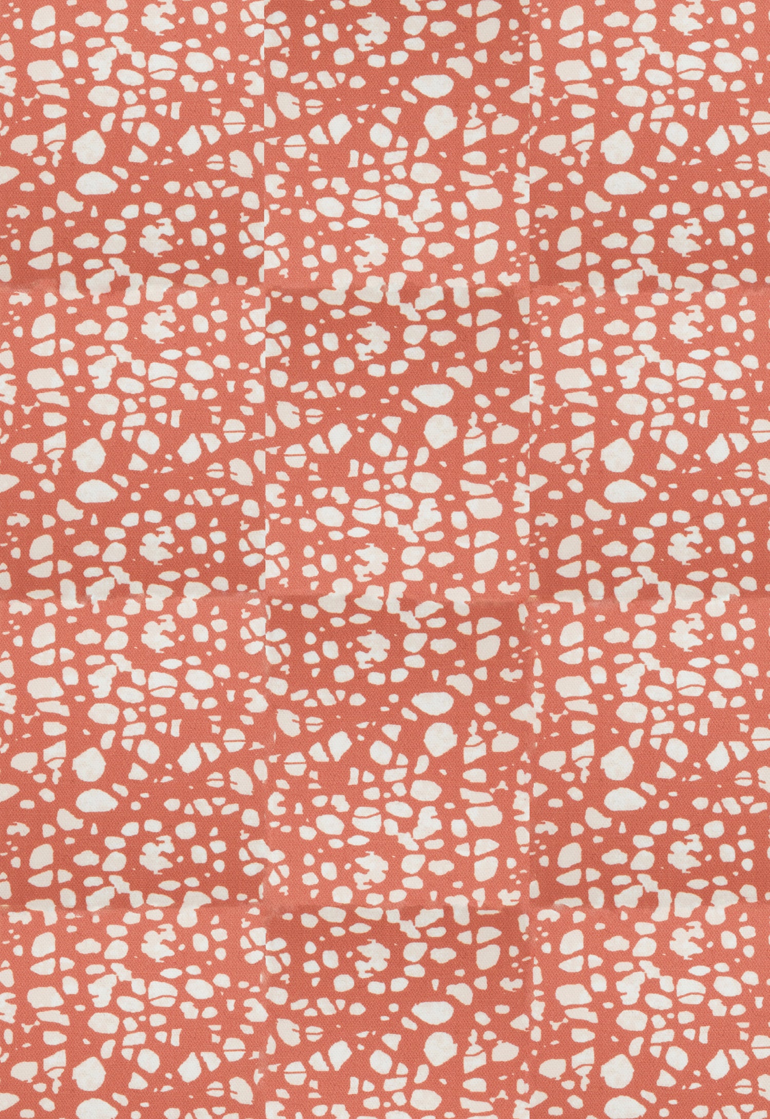 Detail of fabric in a batik splatter print in cream on a coral field.