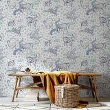 A bench and basket stand in front of a wall papered in a playful hand-drawn animal print in shades of blue on a white field.