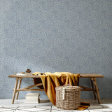 A bench and basket stand in front of a wall papered in a painterly abstract print in white on a light blue field.