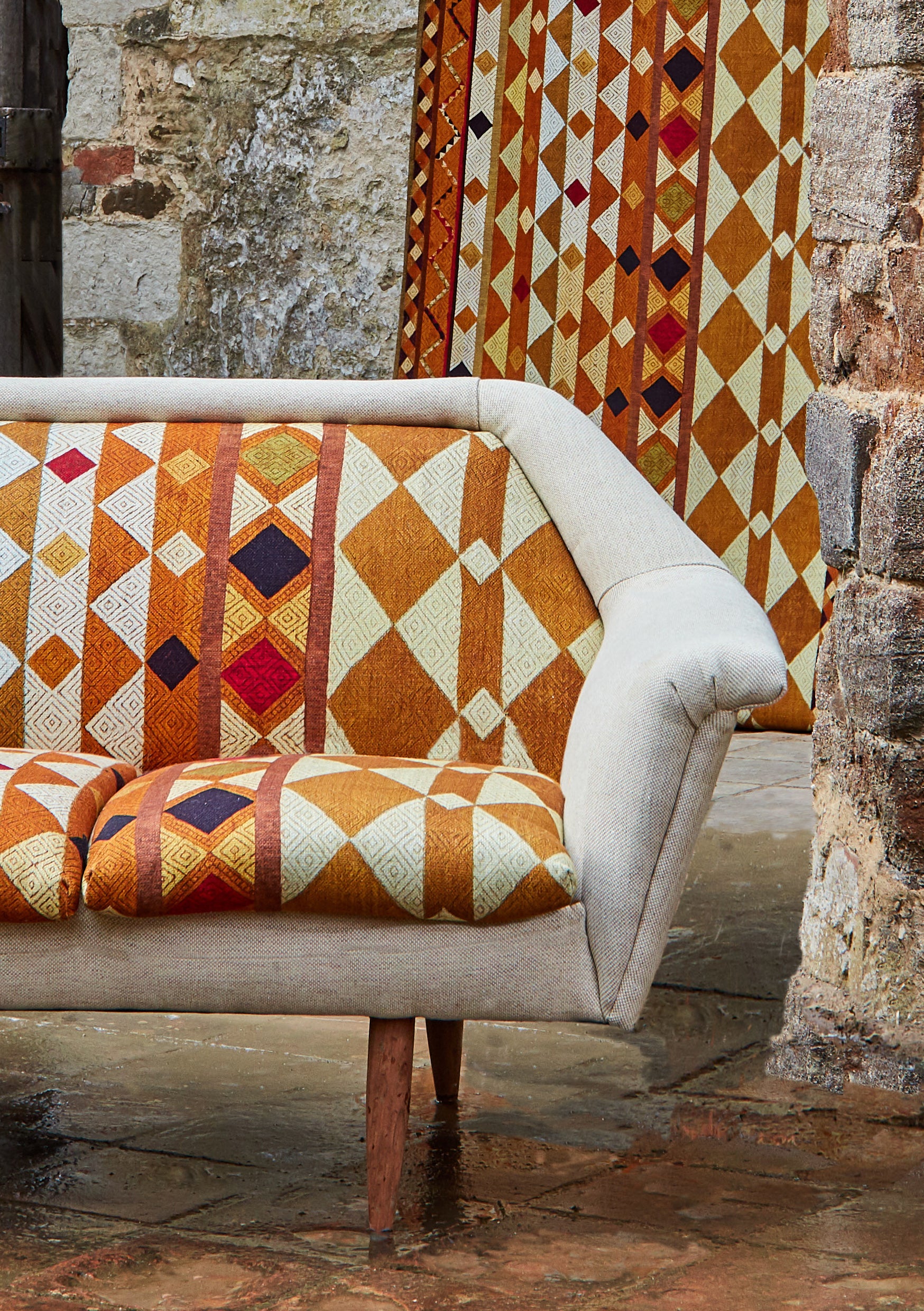 A couch upholstered in a global geometric print in shades of orange, yellow, brown and red.