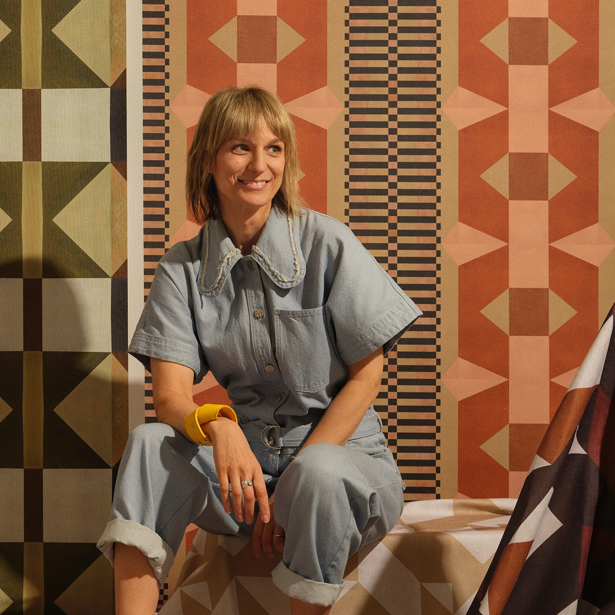 Portait of a blonde woman in a denim jumpsuit, against a colorful geometric background