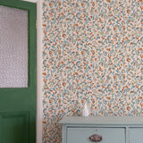 Floral wallpaper with a green door and gray dresser in the corner.