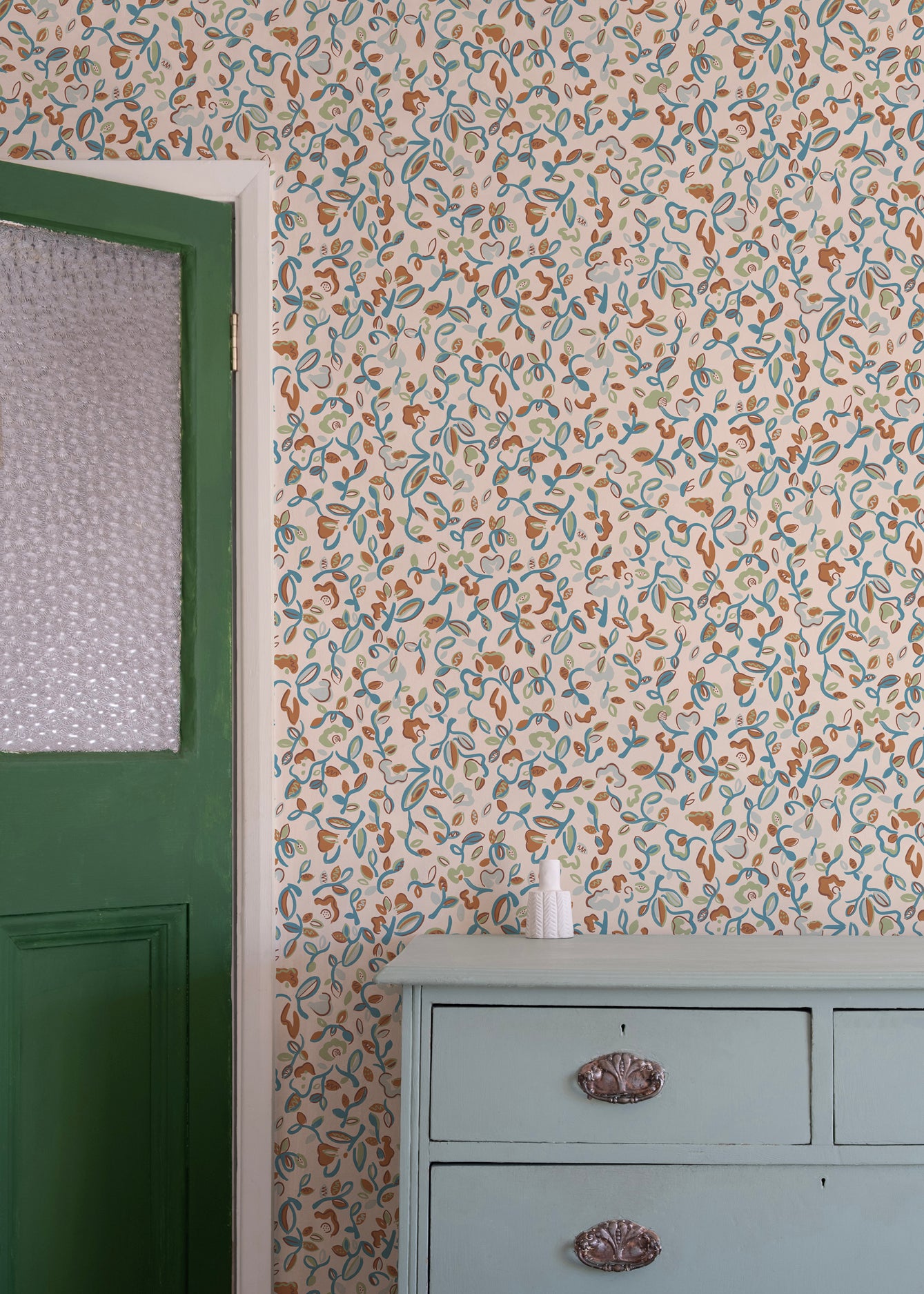 Floral wallpaper with a green door and gray dresser in the corner.