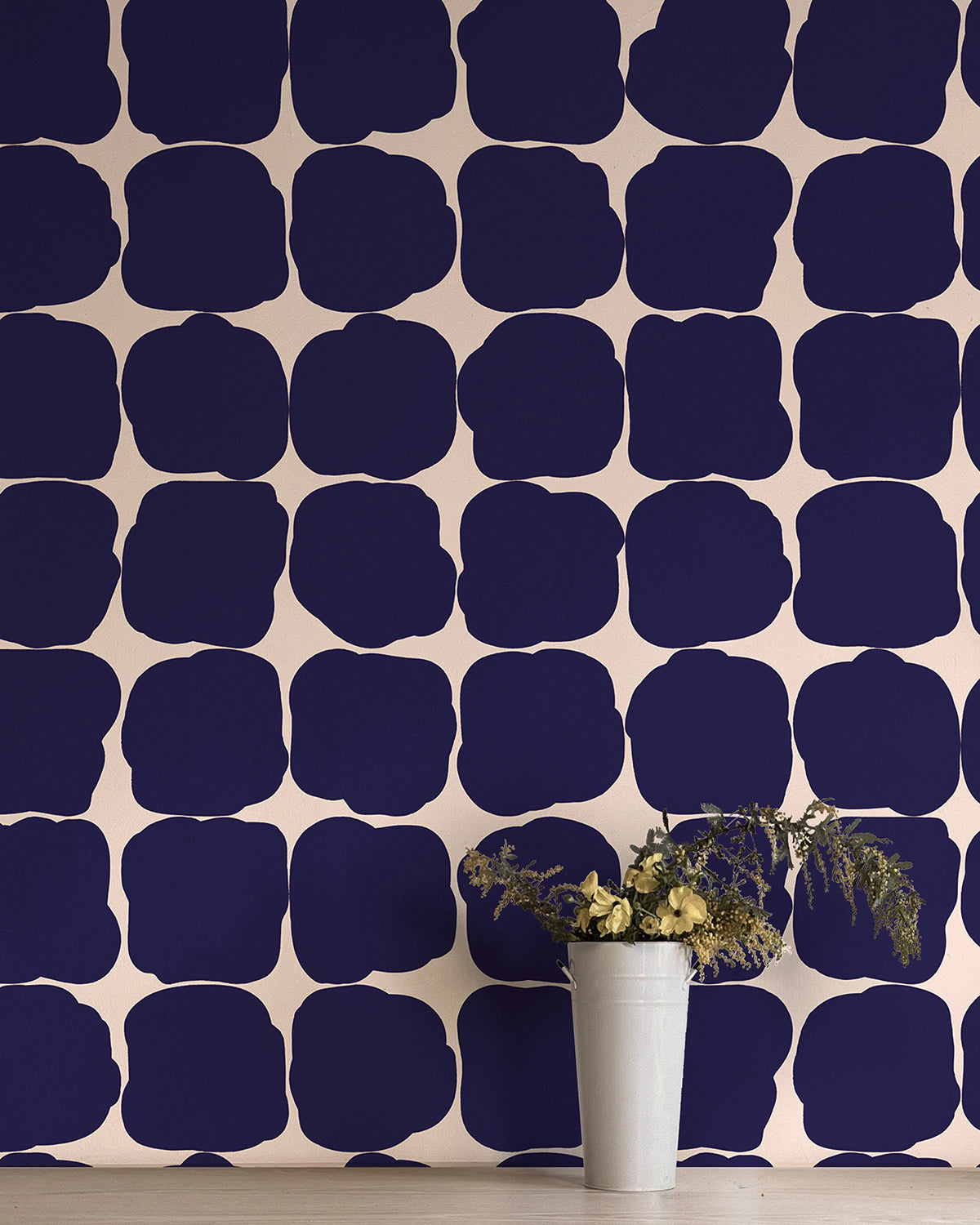 A vase in front of a wall papered in a repeating blot print in dark blue on a cream field.