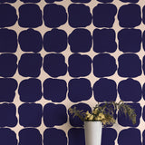 A vase in front of a wall papered in a repeating blot print in dark blue on a cream field.