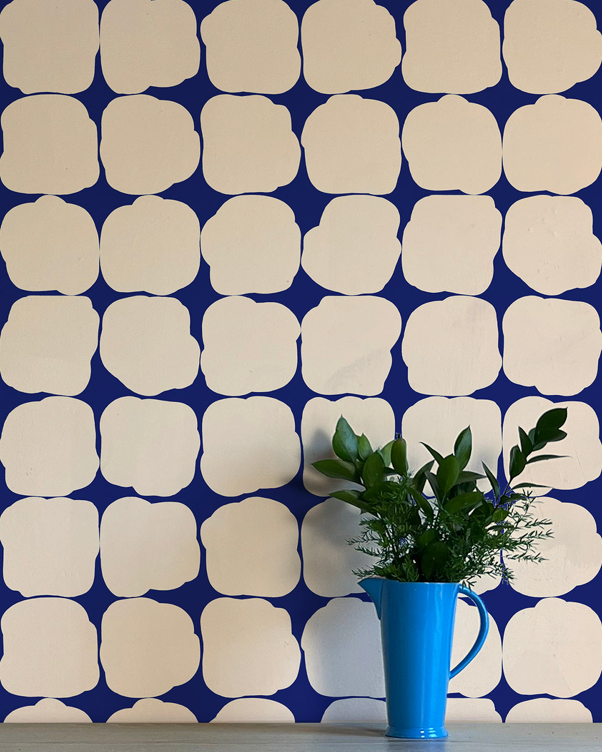 A vase of flowers stands in front of a wall papered in a repeating blot print in cream on a navy field.