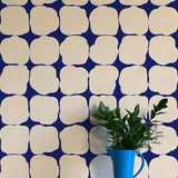 A vase of flowers stands in front of a wall papered in a repeating blot print in cream on a navy field.