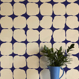 A vase in front of a wall papered in a repeating blot print in cream on a dark blue field.