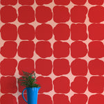 A vase of flowers stands in front of a wall papered in a repeating blot print in red on a pink field.