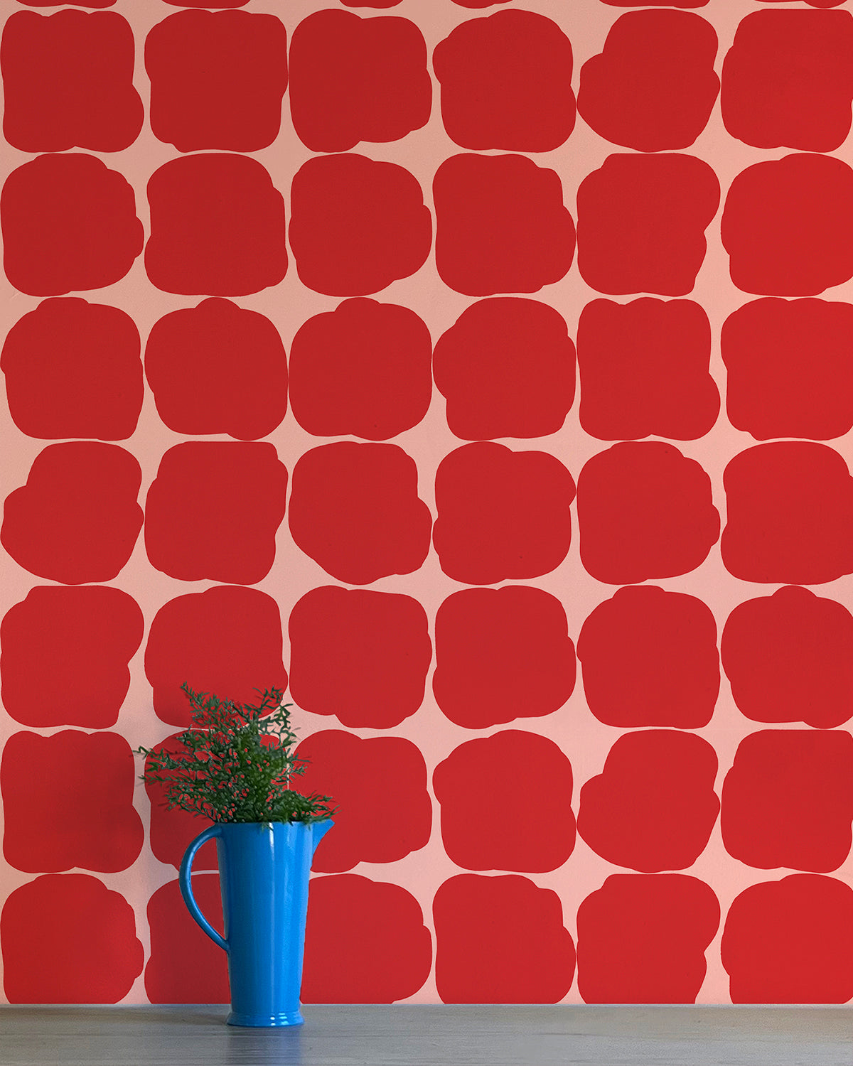 A vase of flowers stands in front of a wall papered in a repeating blot print in red on a pink field.