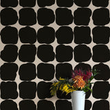 A vase of flowers stands in front of a wall papered in a repeating blot print in black on a white field.