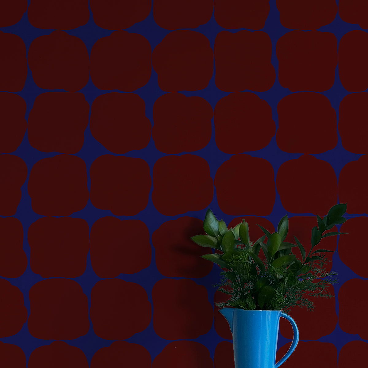 A vase of flowers stands in front of a wall papered in a repeating blot print in maroon on a blue field.