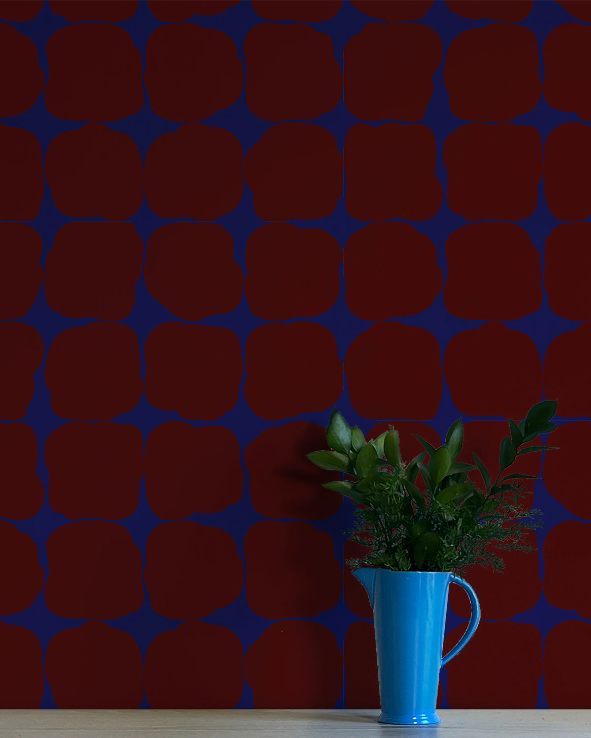 A vase of flowers stands in front of a wall papered in a repeating blot print in maroon on a blue field.