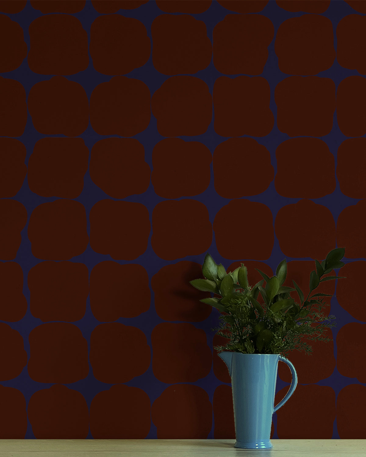 A vase of flowers stands in front of a wall papered in a repeating blot print in deep red on a dark blue field.