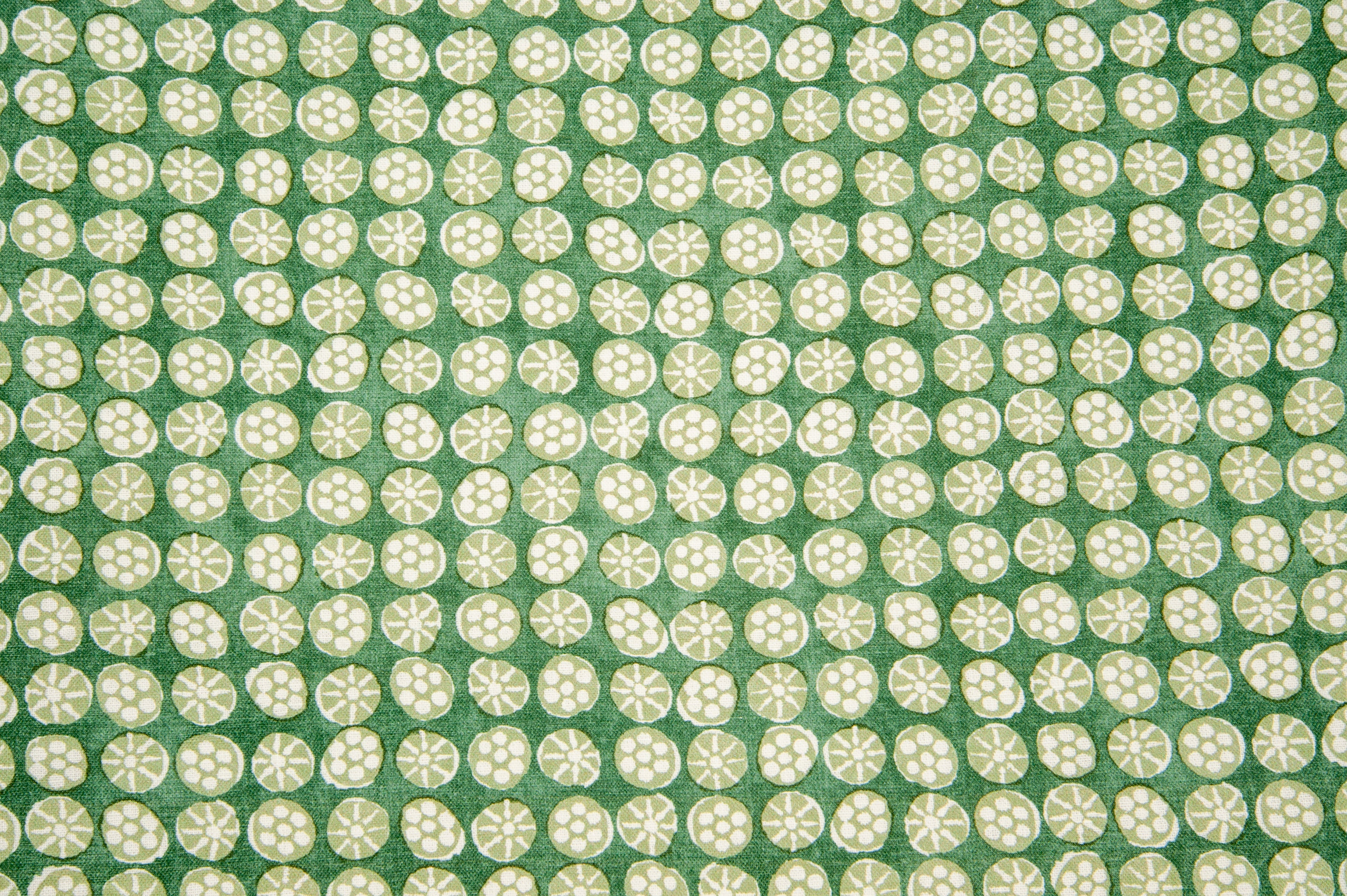 Detail of fabric in a circular floral print in light green and white on a mottled green field.