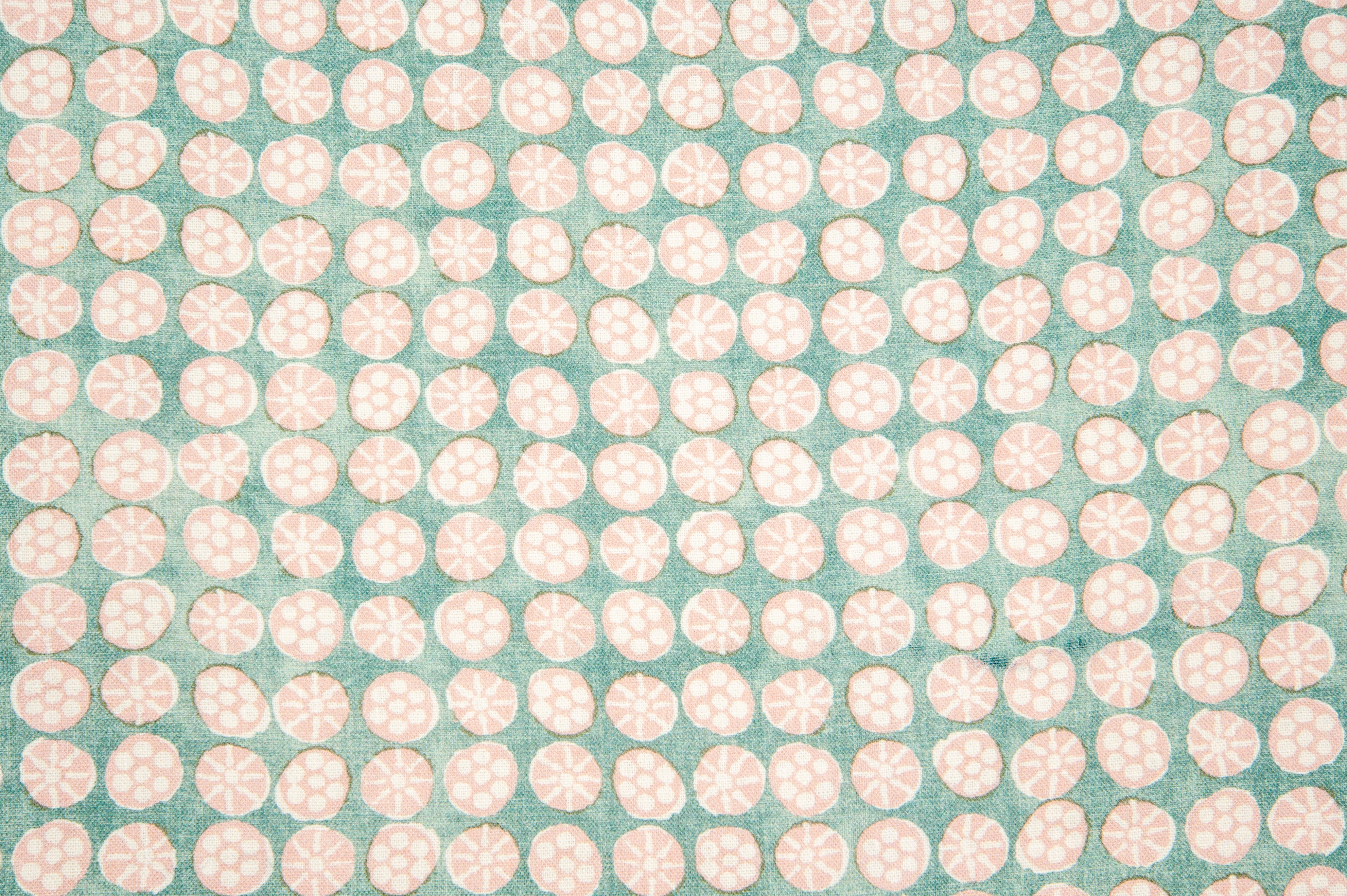 Detail of fabric in a circular floral print in light pink and white on a mottled turquoise field.