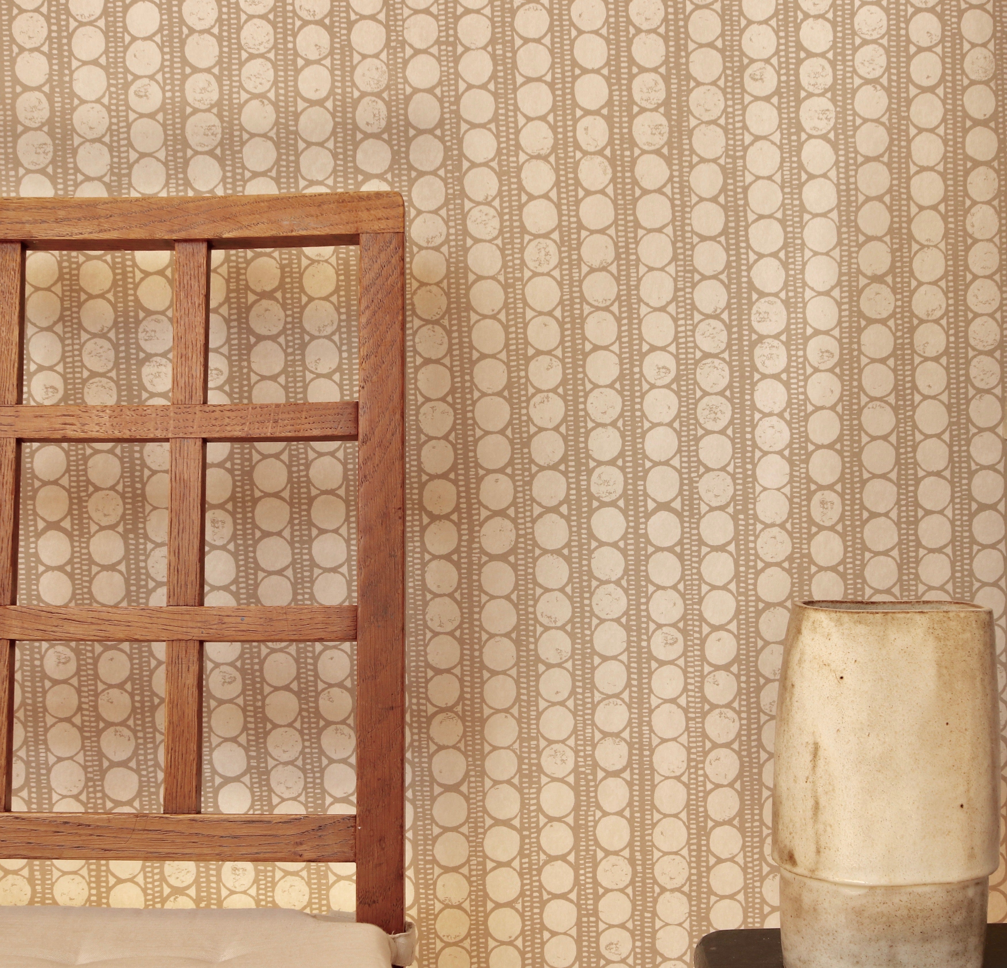 A wooden chair and ceramic vase against wallpaper in a circle and stripe print in white on a oatmeal field.