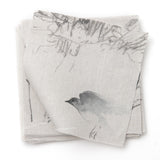 A stack of linen fabric swatches in a painterly bird and branch print in shades of gray on a cream field.