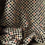Draped jacquard fabric in a checked pattern in shades of yellow, pink, purple and black on a tan field.