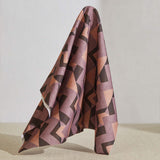 A large piece of draped fabric in a dense geometric print in shades of peach, brown and purple.