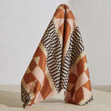 A large piece of draped fabric in a dense geometric print in shades of pink, orange and brown on a cream field.