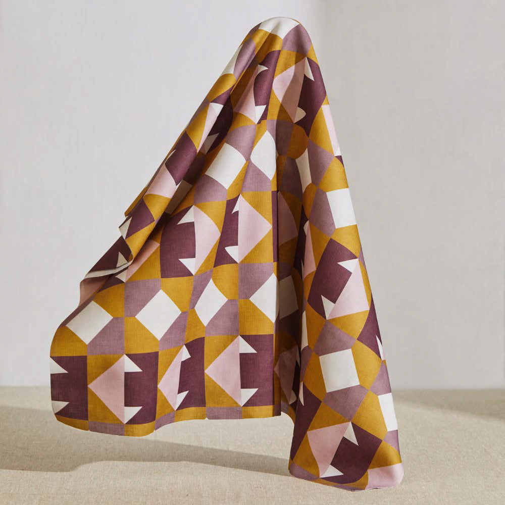 A large piece of draped fabric in a geometric grid print in mustard, pink and purple on a white field.