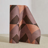 A curved partition stands on the ground, covered in a dense geometric print in peach, purple and brown.