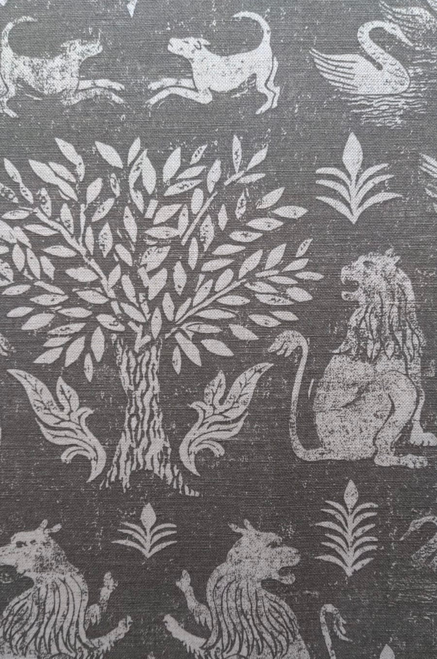 Close-up of fabric in a lion and plant print in white on a mottled gray field.