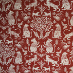 Detail of fabric in a lion and plant print in white on a mottled red field.