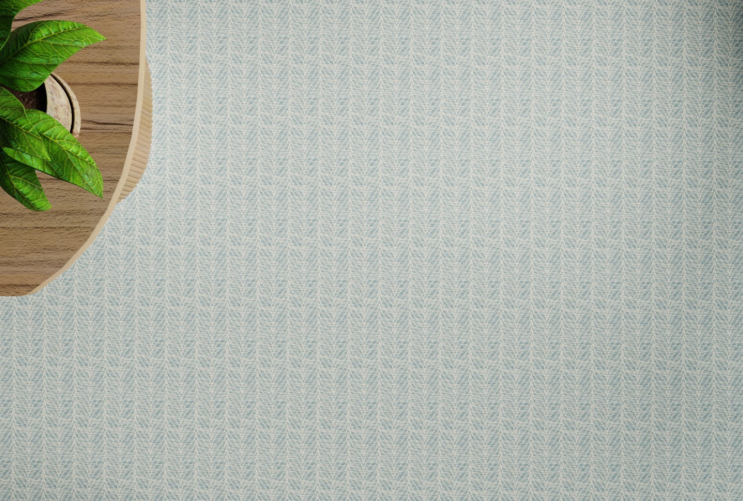 Overhead image of a wooden table and plant on a broadloom carpet in a textural herringbone pattern in cream and pastel blue. 