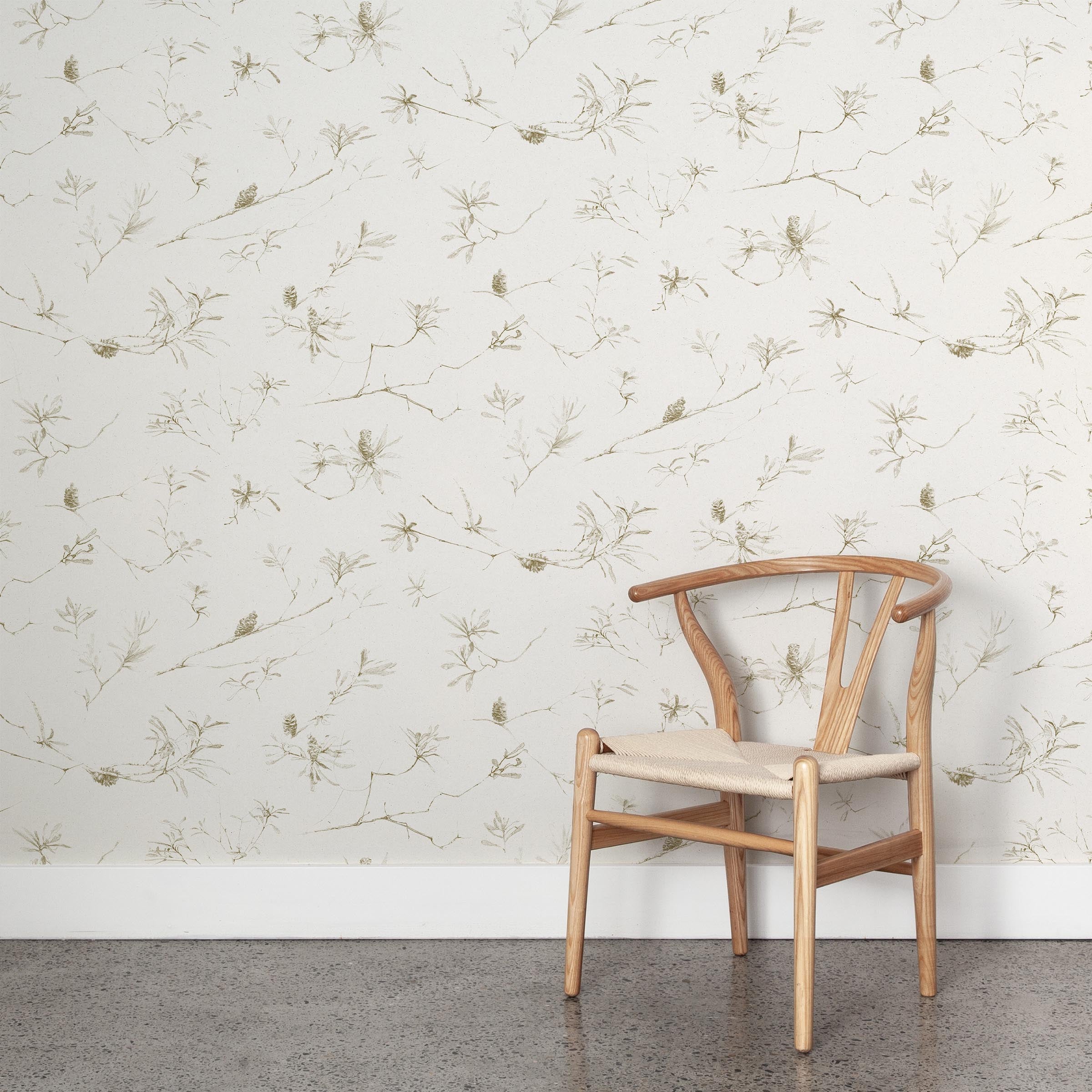 A wooden chair stands in front of a wall papered in a painterly pine cone and branch print in green on a cream field.