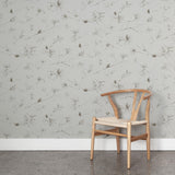 A wooden chair stands in front of a wall papered in a painterly pine cone and branch print in gray on a greige field.