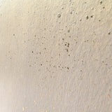 Wide-angle shot of wallpaper in a random splattered pattern in metallic gold on a cream field.