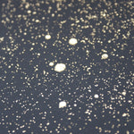 Wide-angle shot of wallpaper in a random splattered pattern in metallic gold on a black field.