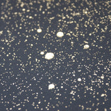 Wide-angle shot of wallpaper in a random splattered pattern in metallic gold on a black field.