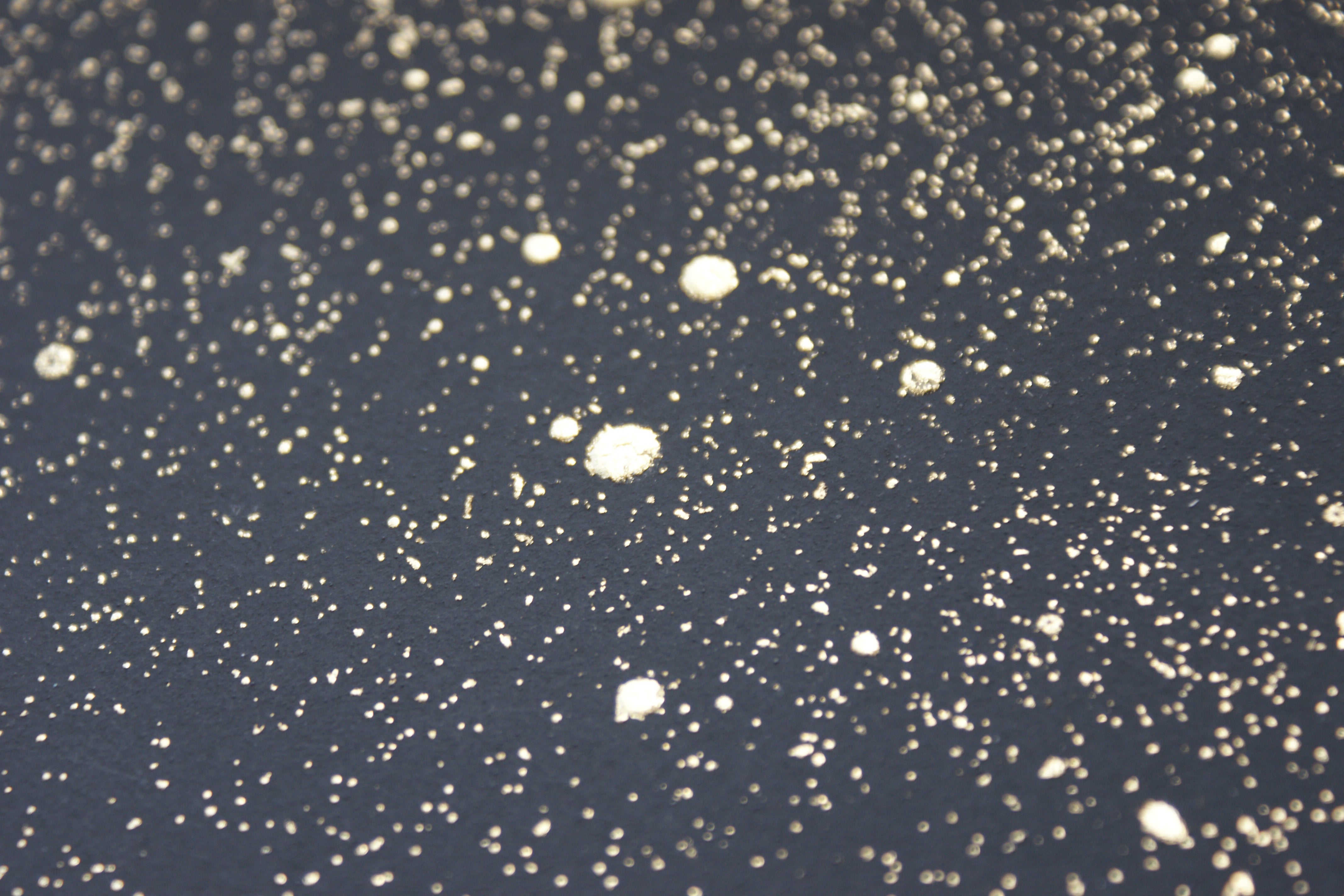 Wide-angle shot of wallpaper in a random splattered pattern in metallic gold on a black field.